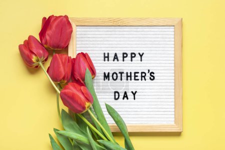 Téléchargez les photos : Feutre avec texte Happy Mothers day, bouquet de tulipes rouges sur fond jaune carte de vœux de fin d'année Flat lay Vue du dessus. - en image libre de droit
