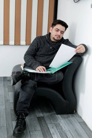 Photo for A young employee is sitting on couch and holding paper in hand. - Royalty Free Image