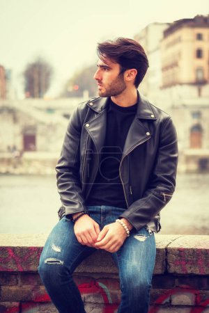 Photo of a stylish man leaning on a fence in a leather jacket