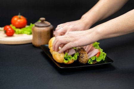 Picture of woman hands preparing tasty sandwiches with ham, cheese and vegetables in black plate