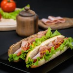 Still life with tasty sandwiches with ham, cheddar and vegetables in black plate on a black background