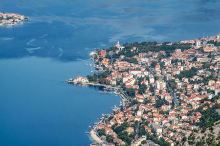 Amazing view from above of motor boats in the sky blue sea of the Bay of Kotor in Montenegro, with a picturesque coastline, red roofs of houses and the marina with boats.