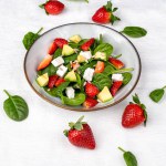Summer fresh salad with strawberry, baby spinach, avocado and feta cheese in a plate on white background. Concept of health food.