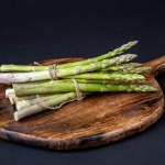 A bunch of fresh asparagus over a wooden board on a black background. Healthy food. 	