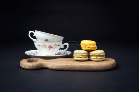 Photo for Still life with pistachios and orange macaroons arranged with beautiful fine porcelain in baroque style on a black background - Royalty Free Image