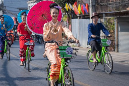 Photo for Chiang Mai, Thailand - January 20, 2023: Pretty women holding beautiful umbrellas in traditional costumes and riding cycling bicycles annual show at San Kamphaeng, Bosang umbrella festival. - Royalty Free Image