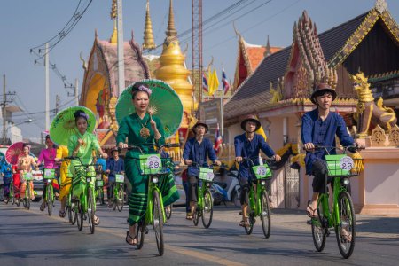 Foto de Chiang Mai, Thailand - January 20, 2023: Pretty women holding beautiful umbrellas in traditional costumes and riding cycling bicycles annual show at San Kamphaeng, Bosang umbrella festival. - Imagen libre de derechos