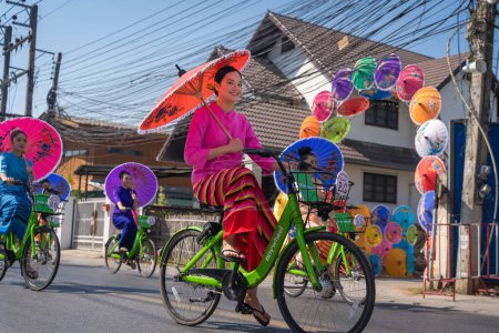 Photo for Chiang Mai, Thailand - January 20, 2023: Pretty women holding beautiful umbrellas in traditional costumes and riding cycling bicycles annual show at San Kamphaeng, Bosang umbrella festival. - Royalty Free Image