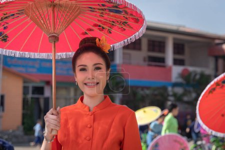 Foto de Chiang Mai, Thailand - January 20, 2023: Pretty women holding beautiful umbrellas in traditional costumes smiled at the participants of the annual event show San Kamphaeng, Bo sang umbrella festival. - Imagen libre de derechos