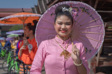 Foto de Chiang Mai, Tailandia - 20 de enero de 2023: Mujeres guapas sosteniendo hermosos paraguas con trajes tradicionales sonrieron a los participantes del evento anual San Kamphaeng, Bo cantó el festival de paraguas. - Imagen libre de derechos