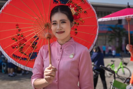 Téléchargez les photos : Chiang Mai, Thaïlande - 20 janvier 2023 : De jolies femmes tenant de beaux parapluies en costumes traditionnels ont souri aux participants du spectacle annuel San Kamphaeng, Bo a chanté le festival de parapluie. - en image libre de droit