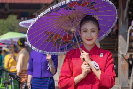 Foto de Chiang Mai, Tailandia - 20 de enero de 2023: Mujeres guapas sosteniendo hermosos paraguas con trajes tradicionales sonrieron a los participantes del evento anual San Kamphaeng, Bo cantó el festival de paraguas. - Imagen libre de derechos