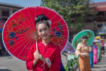Photo for Chiang Mai, Thailand - January 20, 2023: Pretty women holding beautiful umbrellas in traditional costumes smiled at the participants of the annual event show San Kamphaeng, Bo sang umbrella festival. - Royalty Free Image