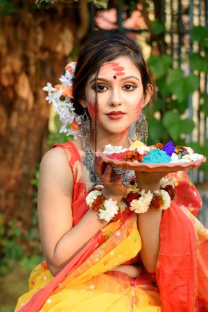 Foto de Retrato de una hermosa joven india vestida con saris y joyas tradicionales, sosteniendo colores en polvo en plato en el festival de colores llamado Holi, un popular festival hindú celebrado en toda la India.. - Imagen libre de derechos