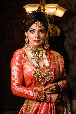 Magnífica joven novia india en traje de novia de lujo con maquillaje y joyas pesadas con interior clásico vintage en iluminación de estudio. Moda de boda y estilo de vida.