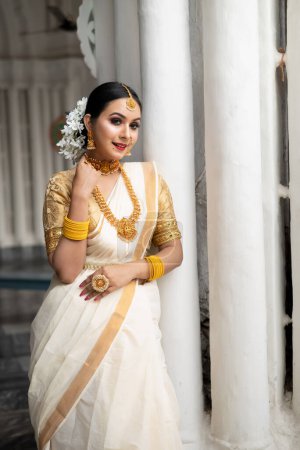Foto de Impresionante novia vestida con un saree tradicional de novia india con joyas de oro sonríe tiernamente frente a un fondo vintage. Boda moda y estilo de vida. - Imagen libre de derechos