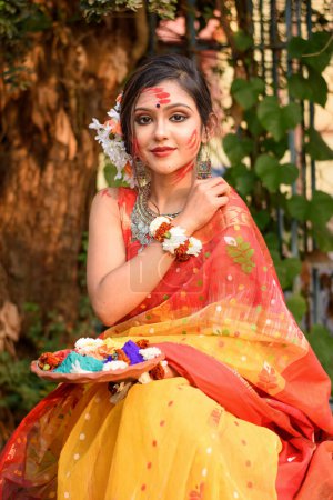 Porträt eines hübschen jungen Mädchens, das traditionellen indischen Sari und Schmuck trägt und Puderfarben in Tellern auf dem Holi-Fest hält, einem beliebten hinduistischen Fest, das in ganz Indien gefeiert wird..