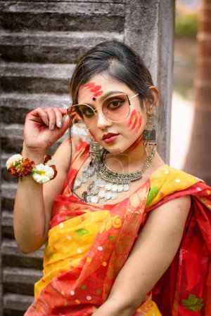 Portrait de jolie jeune fille portant saree et bijoux indiens traditionnels, jouant avec les couleurs et posant à la mode avec des lunettes de soleil sur le festival des couleurs appelé Holi.
