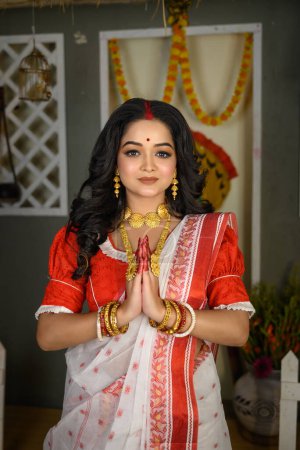 Porträt einer schönen jungen indischen Frau in traditionellem Sari, Goldschmuck und Armreifen, die eine Namaskar-Pose einnimmt. Maa Durga agomoni schießen Konzept.