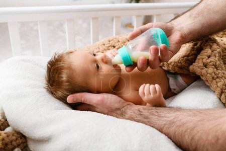 Téléchargez les photos : Père poilu mains nourrissent le nourrisson avec des préparations lactées à partir de biberon en plastique, bébé nouveau-né préparer à la sieste sommeil - en image libre de droit