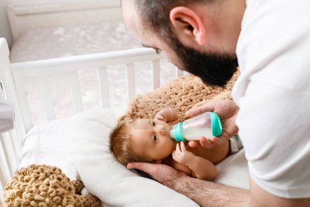 Téléchargez les photos : Père nourrissent le nourrisson endormi avec la formule de lait de bébé du biberon en plastique, se préparent pour la sieste de jour, papa papa soin de famille - en image libre de droit