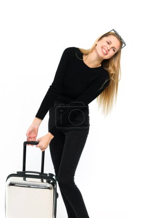 Téléchargez les photos : Jolie jeune femme tirant sa lourde valise sur fond blanc. Fille en vêtements noirs. - en image libre de droit