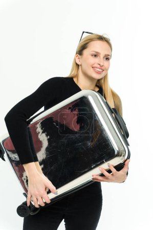 Téléchargez les photos : Jolie jeune femme avec une valise sous le bras sur fond blanc. Fille en vêtements noirs. - en image libre de droit
