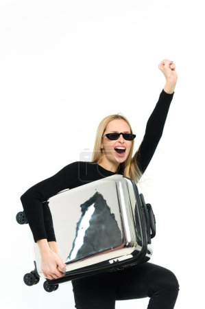 Téléchargez les photos : Jolie jeune femme avec une valise sous le bras sur fond blanc. Fille en vêtements noirs. - en image libre de droit