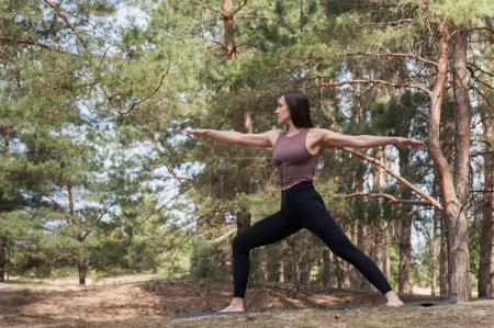 Une jeune femme séduisante en vêtements de sport pratique le yoga dans la forêt. Femme dans une posture de guerrier.