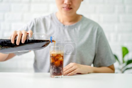 Frau gießt Cola in ein Glas mit Eis.