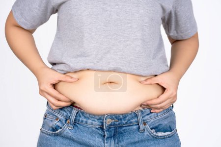 Main de femme tenant ventre sur fond blanc avec espace de copie. Concept d'obésité.
