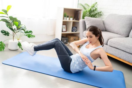 Photo for Asian young healthy woman exercising on yoga mat at home, she is doing a Russian twist. - Royalty Free Image