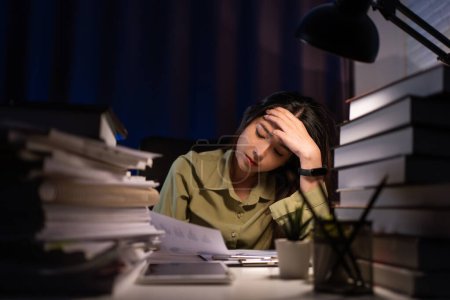 Porträt einer asiatischen Geschäftsfrau, die vor dem Computer sitzt und hart arbeitet und am Arbeitsplatz viele Dokumente auf dem Tisch liegen hat, spät mit ernsthafter Aktion, hart arbeiten und zu spätes Konzept