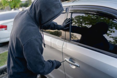 Téléchargez les photos : Un voleur cambriolant une voiture sur le parking. - en image libre de droit