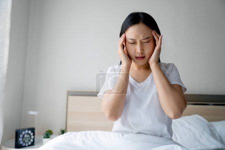 Foto de Mujer asiática con dolor de cabeza tal vez migraña en la mañana en la cama. Ella está masajeando sus templos. - Imagen libre de derechos
