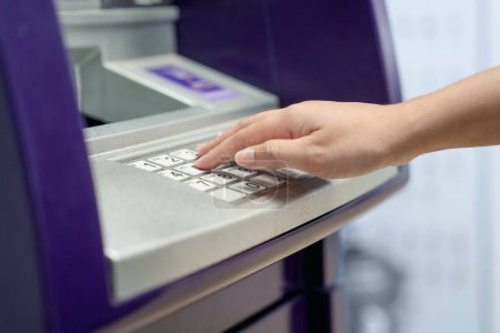 Téléchargez les photos : Femme saisissant son numéro d'identification personnel sur un distributeur automatique. - en image libre de droit