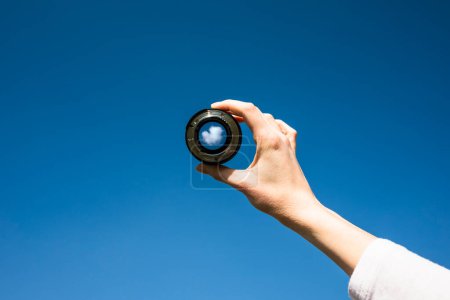 Photo for Woman hand holding a photographic lens aiming at a white cloud in blue sky. Freedom, success, pursue and reach goals concept. - Royalty Free Image