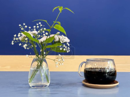 Téléchargez les photos : Tasse à café et pot de fleurs sur la table sur un fond bleu. - en image libre de droit