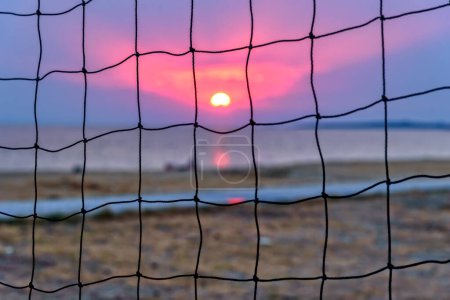 View of the sunset through the volleyball net. Dramatic sunset over sea.