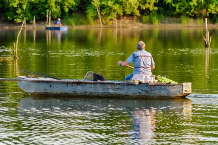 Téléchargez les photos : Novi Sad, Serbie - 06 juillet 2022 : Île du Danube (Sodros) près de Novi Sad, Serbie. Pêcheurs assis dans le bateau et tenant canne à pêche. - en image libre de droit