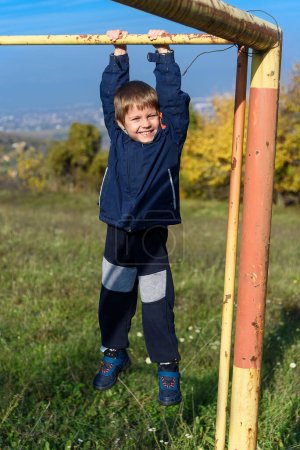 Photo for Kid doing pull ups on sports ground. Boy doing pull ups outdoors. The boy is doing pull-ups - Royalty Free Image