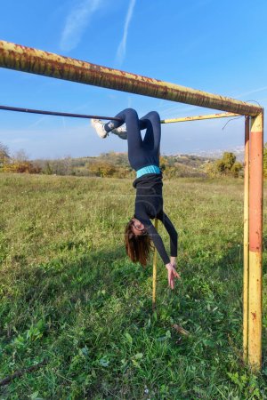 Photo for The girl is hanging by her feet on the pole. Girl doing pull-ups with her legs. Girl hanging upside down on the bar - Royalty Free Image