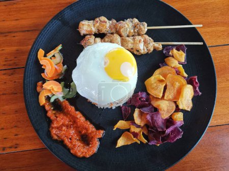 Téléchargez les photos : Fried Rice with chicken satay, egg and Vegetables Nasi Goreng on a black plate - en image libre de droit