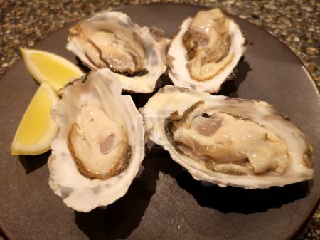 Téléchargez les photos : Oysters with lemon and garlic on a black plate - en image libre de droit