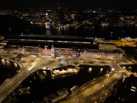 Photo for Amsterdam city center skyline by night aerial drone overhead view. Amsterdam Centraal, Ij, Prins Hendrikkade, public transport, traffic at night. Bright lights urban - Royalty Free Image