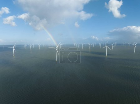 Offshore windpark wind turbine at sea. Electricity generation on open water. WInd water clouds blue sky and a rainbow.