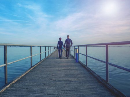 Foto de Pareja woamn y hombre siluetas caminar en muelle muelle sobre el mar. Fantástica mañana con cielo despejado. Puente marítimo de Dranske, Ruegen - Imagen libre de derechos