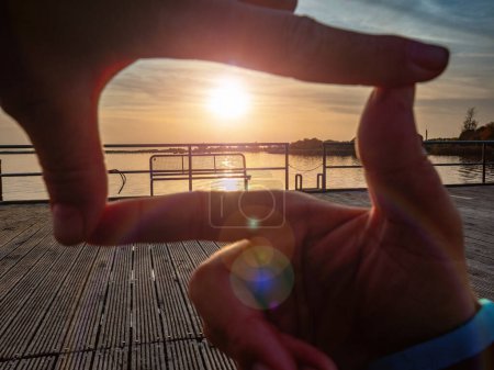 Foto de La mujer mira a través del marco. Gesto formado por dedos sobre el sol poniente en el mar. Destino de enfoque - Imagen libre de derechos