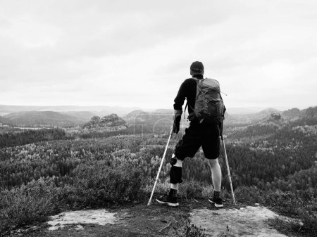 Mann Wanderer mit stützenden Beinschienen und starrte auf die Grausamkeiten. Naturwaldpark im Hintergrund 