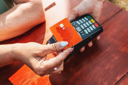 Téléchargez les photos : Femme payer avec carte de crédit. Femme d'âge moyen payant avec carte de crédit dans un café en plein air. - en image libre de droit